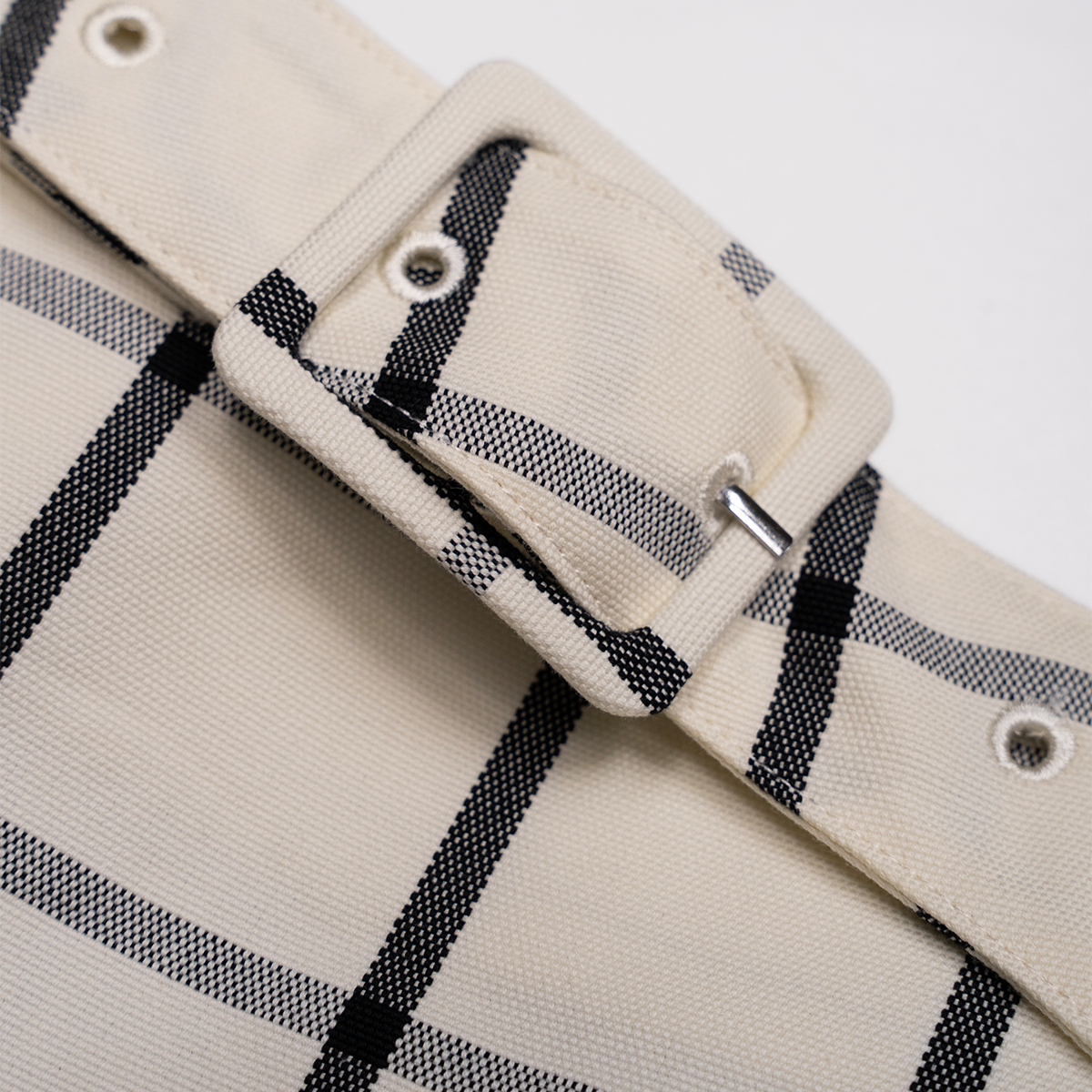 Close-up of a white fabric with black plaid pattern and a matching belt buckle.