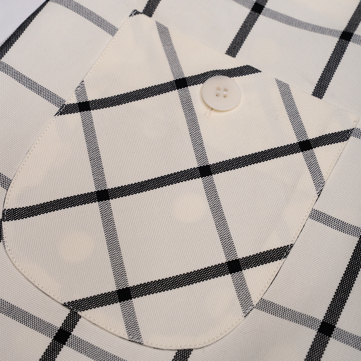 Close-up of a white skirt with black plaid pattern and a button.