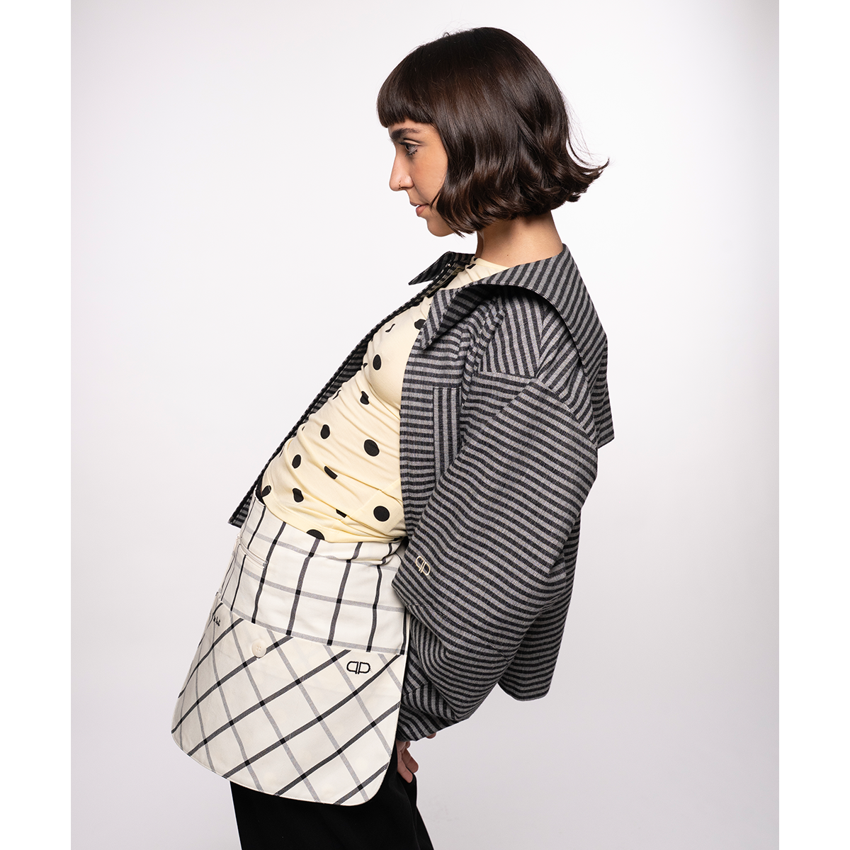 Person wearing a black and white striped jacket with a checkered belt bag on a plain background