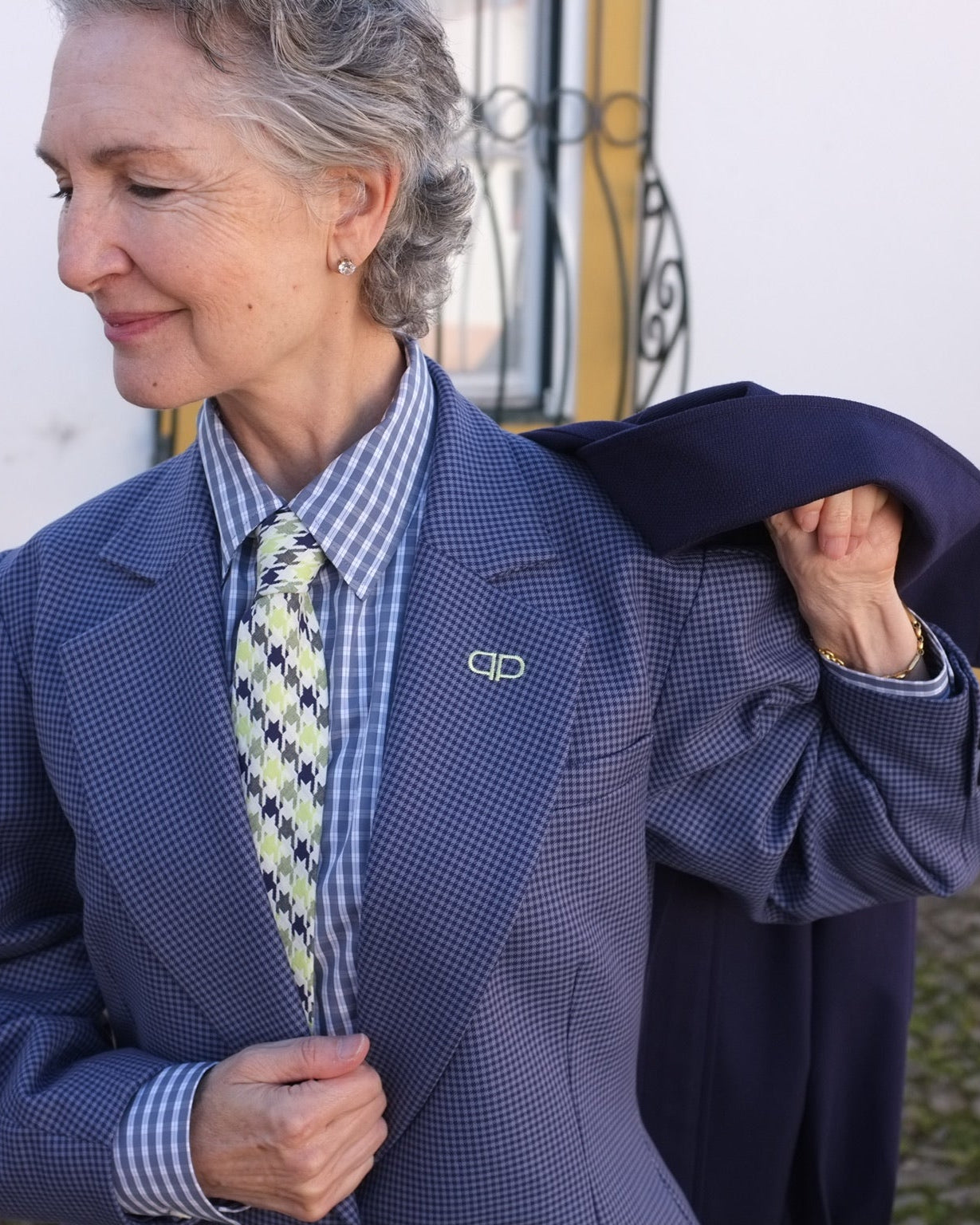 Person wearing a blue checkered suit with a patterned tie, holding a navy coat.