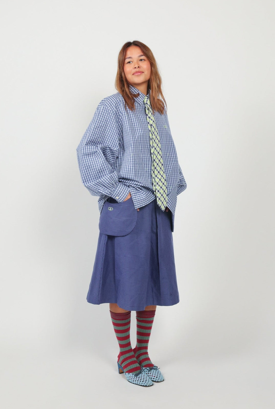 Person wearing a blue checkered shirt, blue skirt, and striped socks on a white background