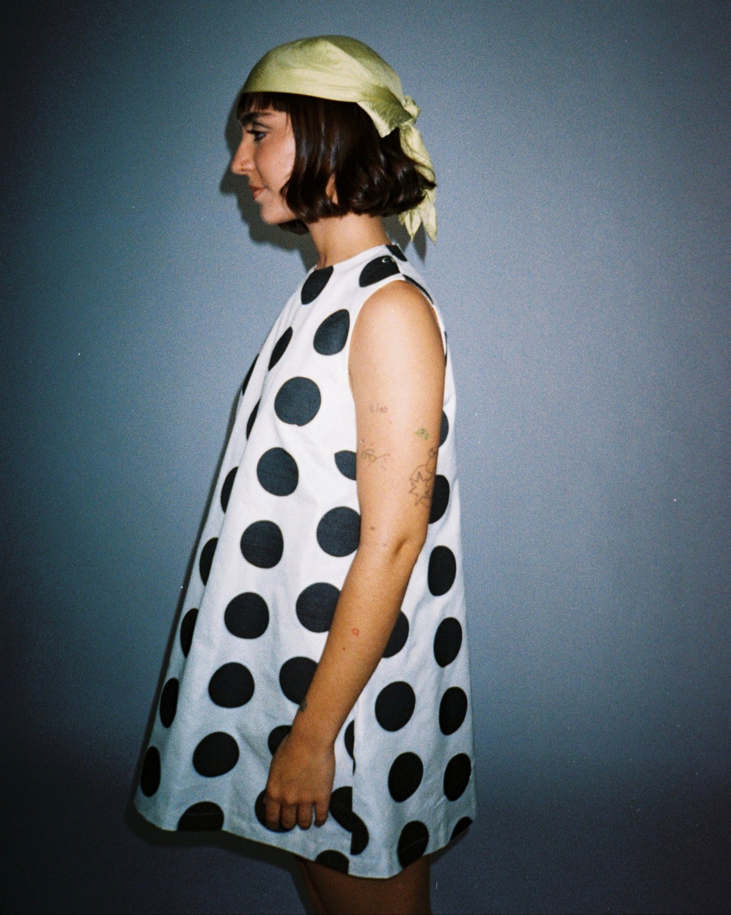 Woman wearing a polka dot dress and headscarf against a plain background