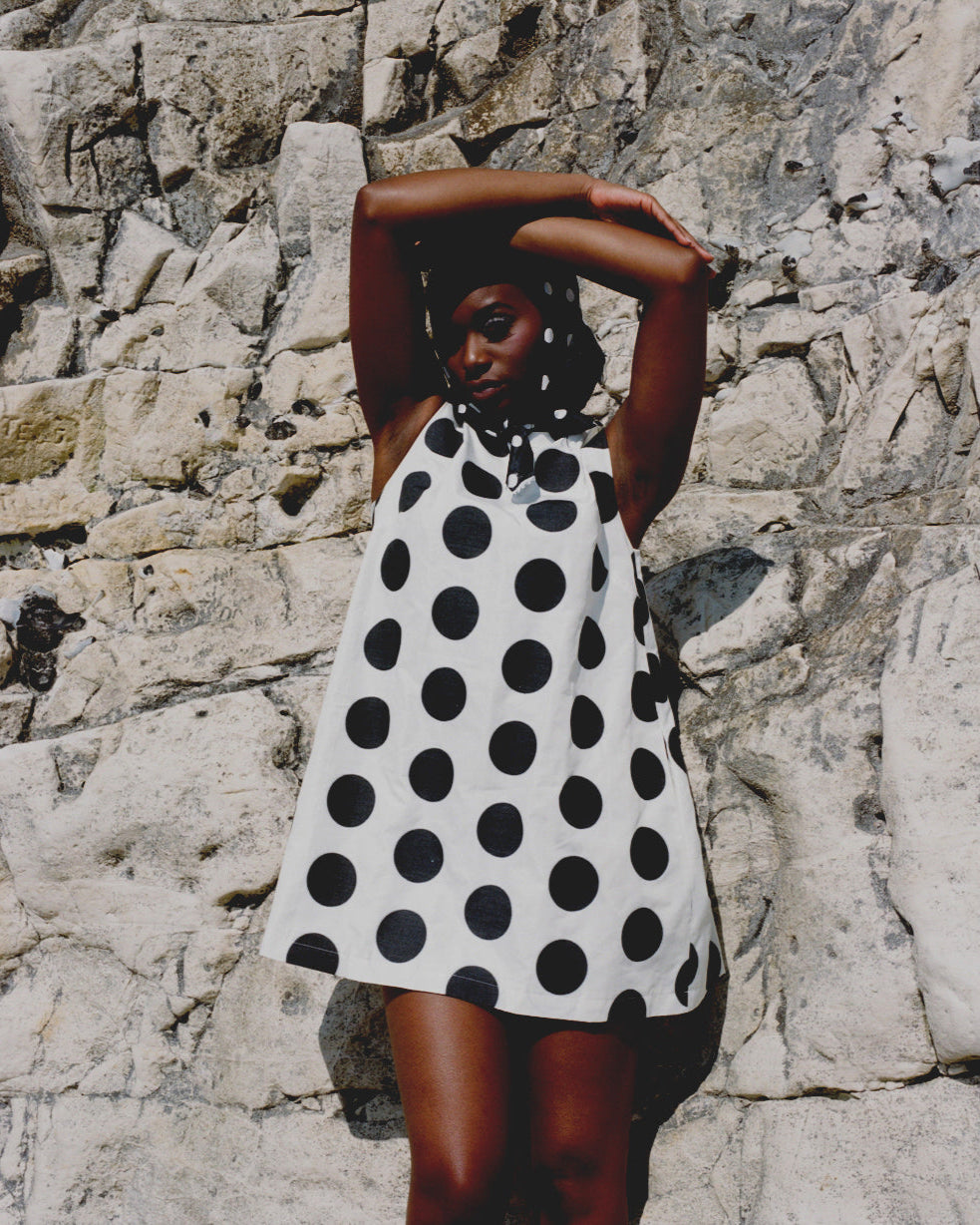Woman wearing a black and white polka dot dress against a stone wall.