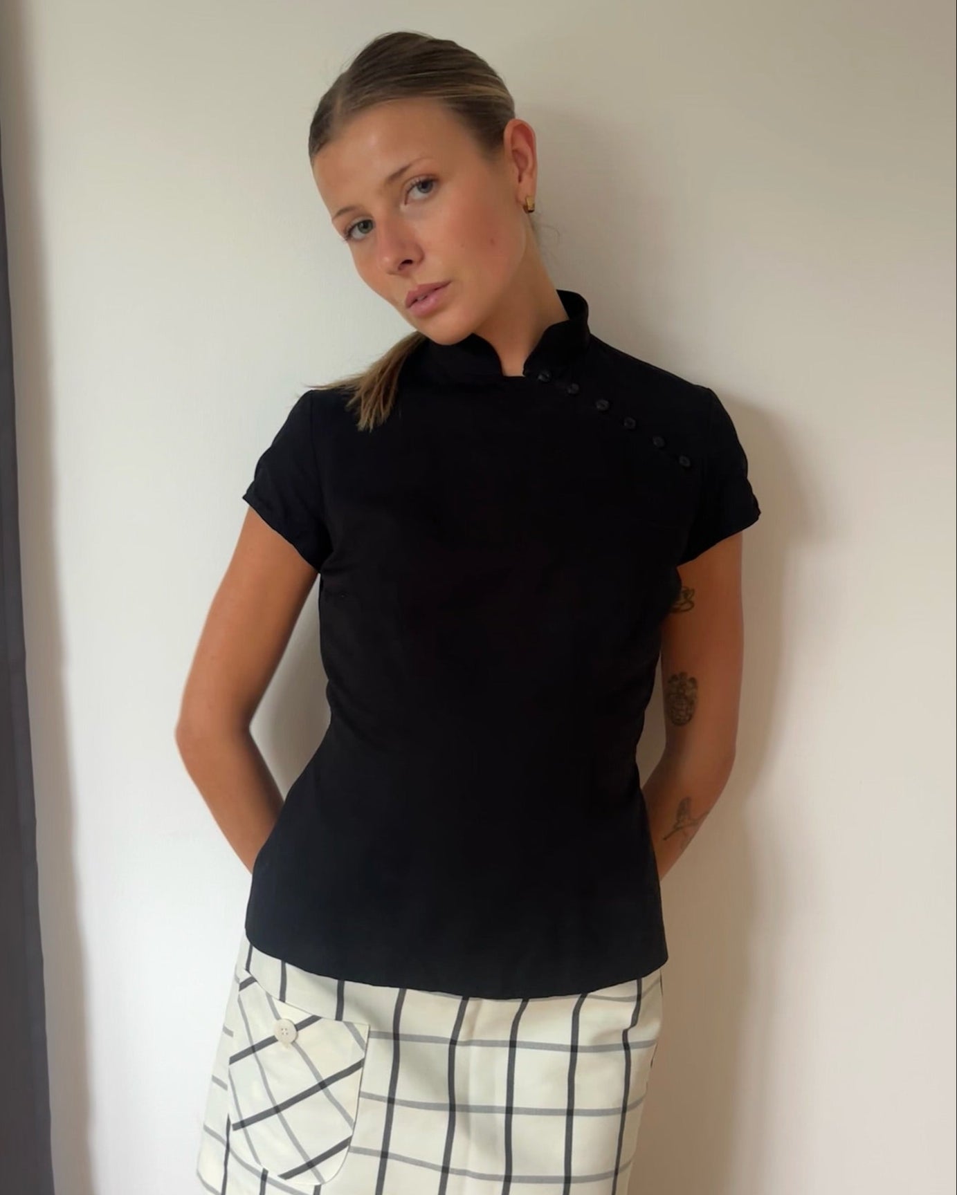 Person wearing a black short-sleeve top and white checkered skirt against a plain background