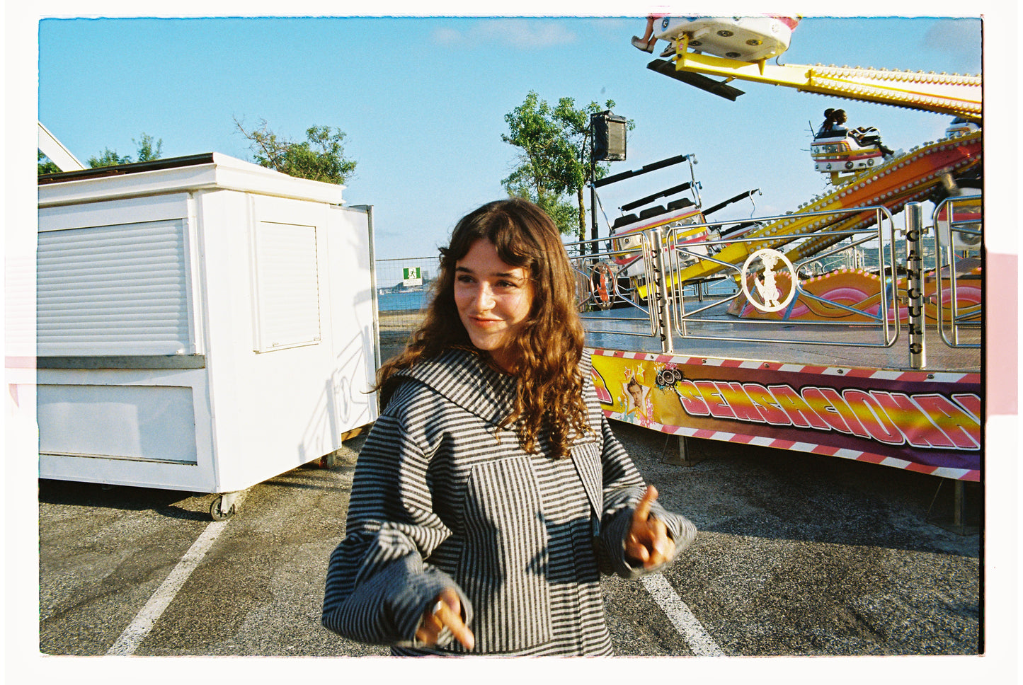Woman standing in front of amusement park rides on a sunny day wearing a striped jacket