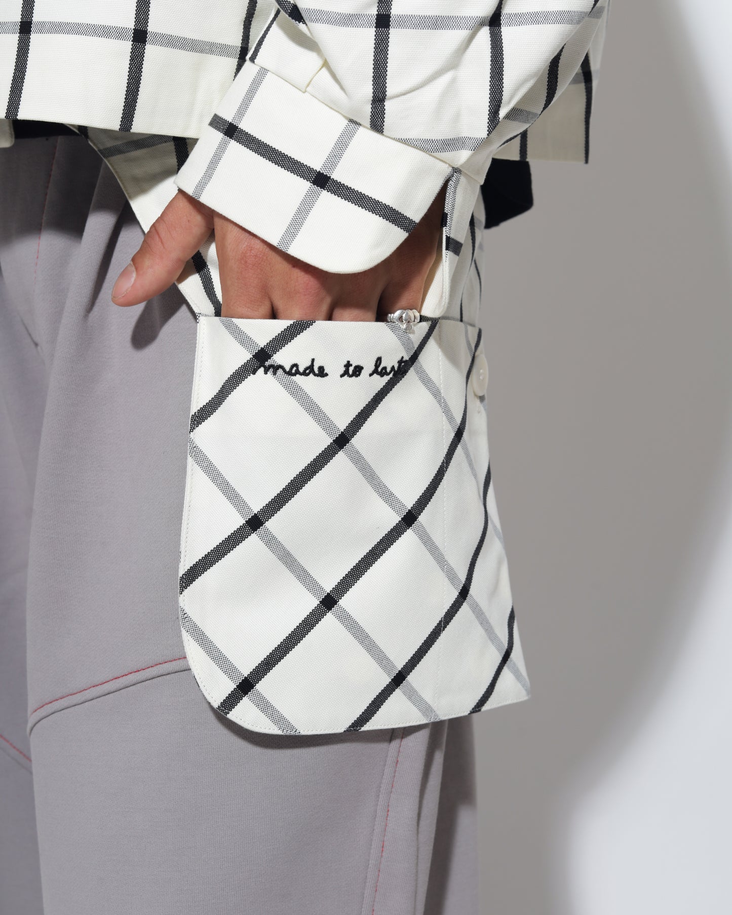 Person wearing a white and black checkered jacket with a matching bag on a plain background
