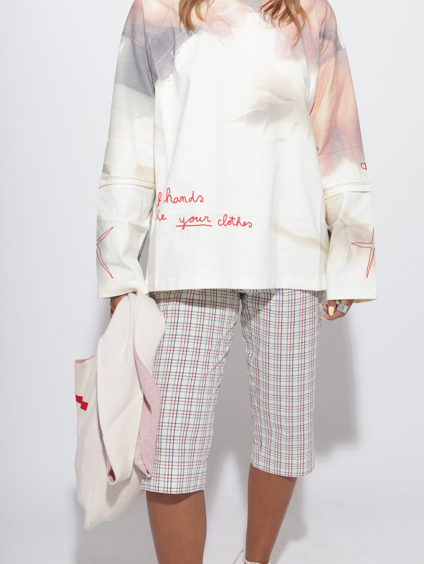 Person wearing a white top with text and plaid capris on a light grey background