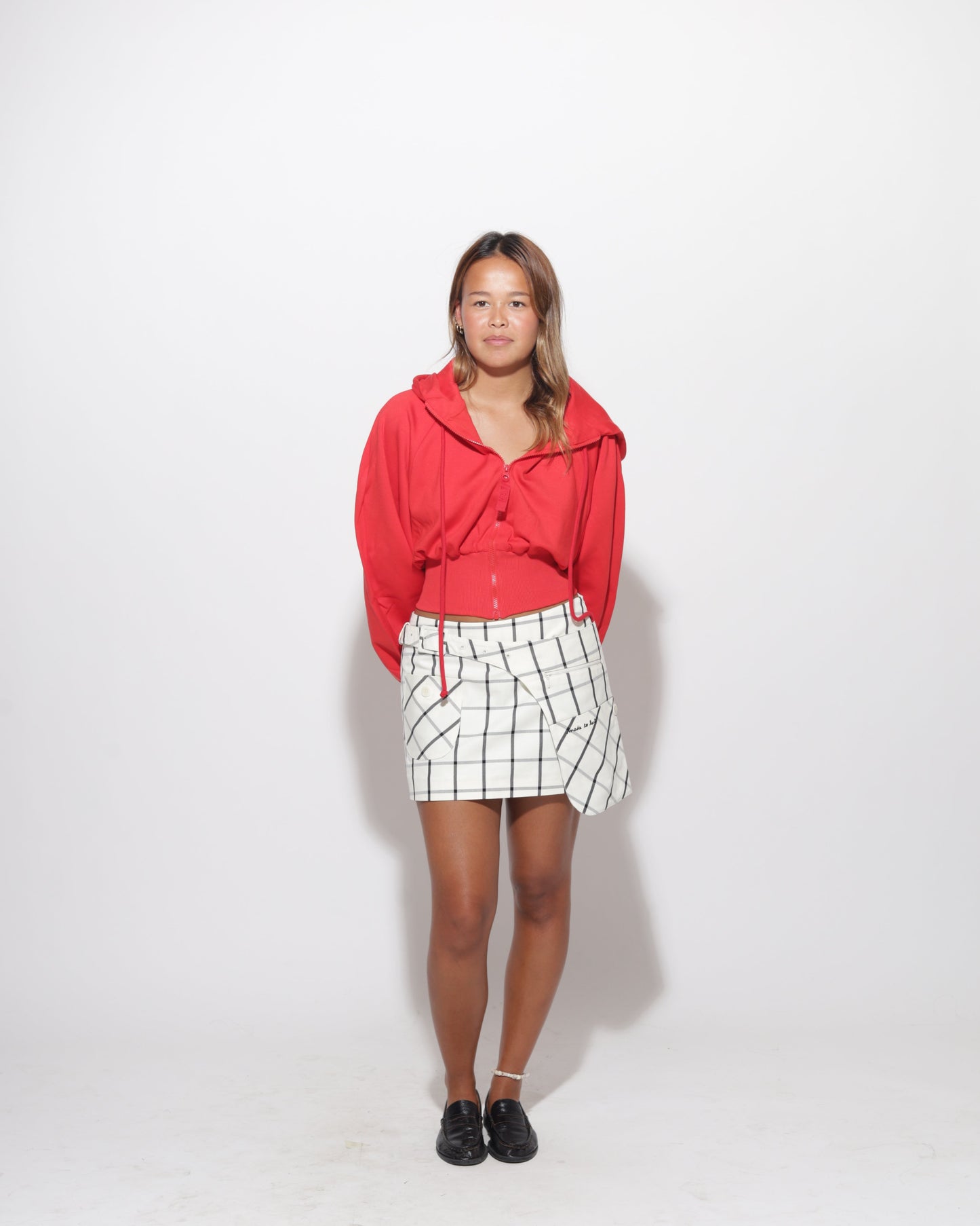Person wearing a red hoodie and plaid skirt on a white background