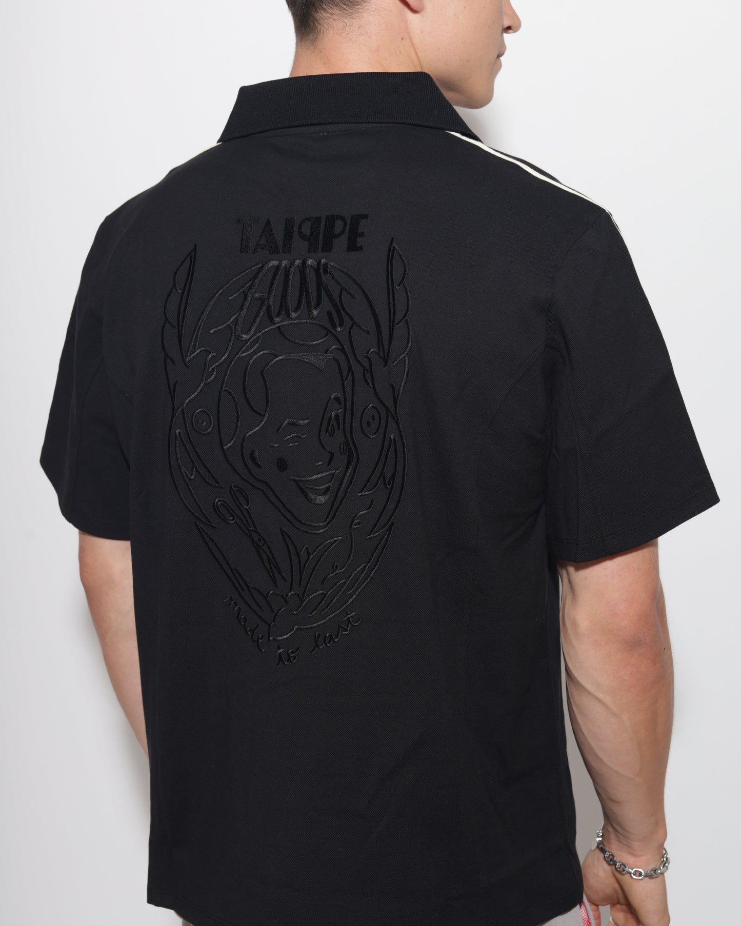 Person wearing a black polo with a logo and text on a white background