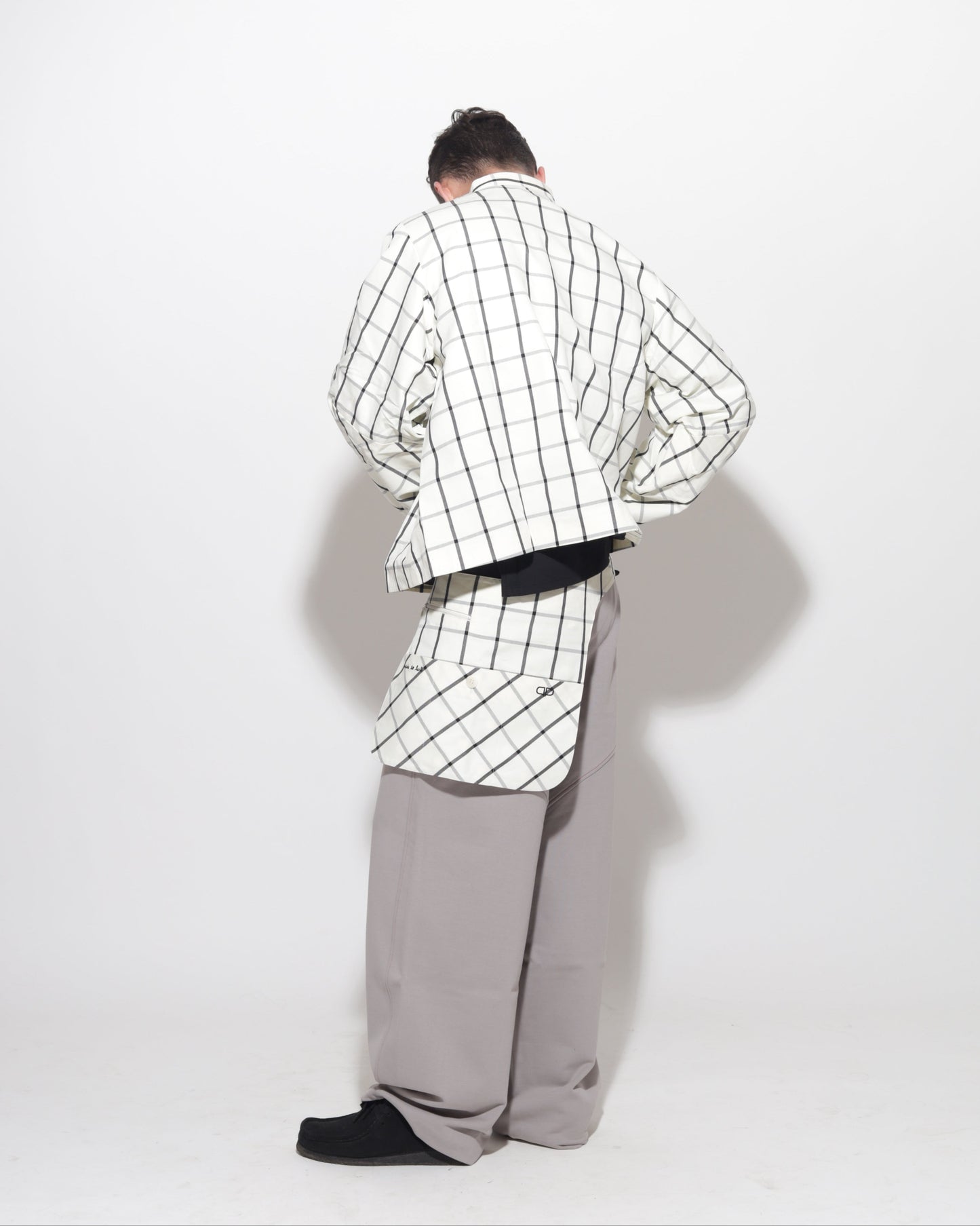 Person wearing a checkered jacket and gray pants on a white background