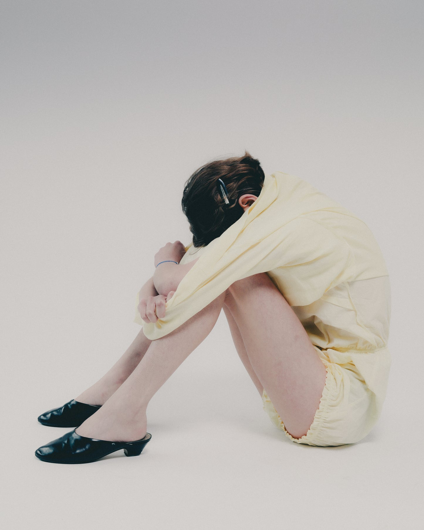 Person sitting on a white background wearing a yellow dress and black shoes.