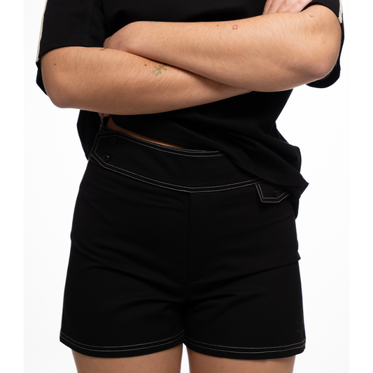 Person wearing black shorts and a black shirt with arms crossed on a white background