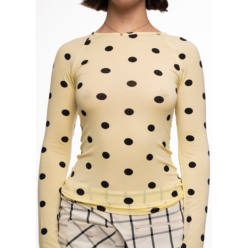 Yellow long-sleeve top with black polka dots worn by a person on a white background