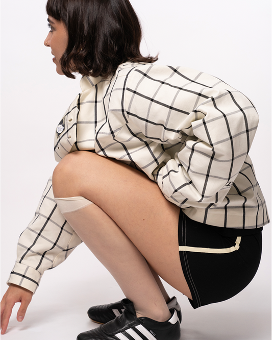 Person wearing a checkered jacket, black shorts, and Adidas shoes on a white background