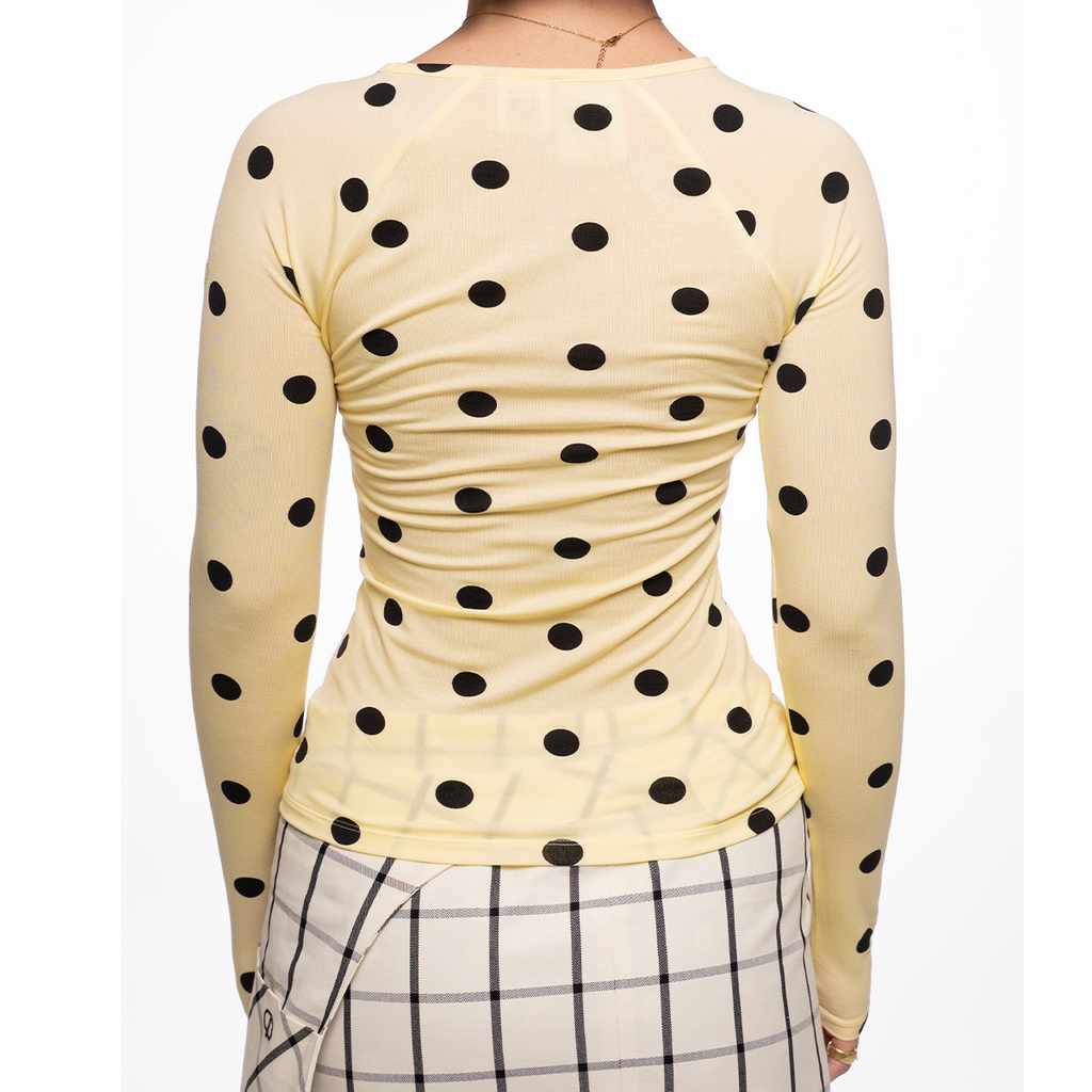 Yellow long-sleeve top with black polka dots worn by a person on a white background