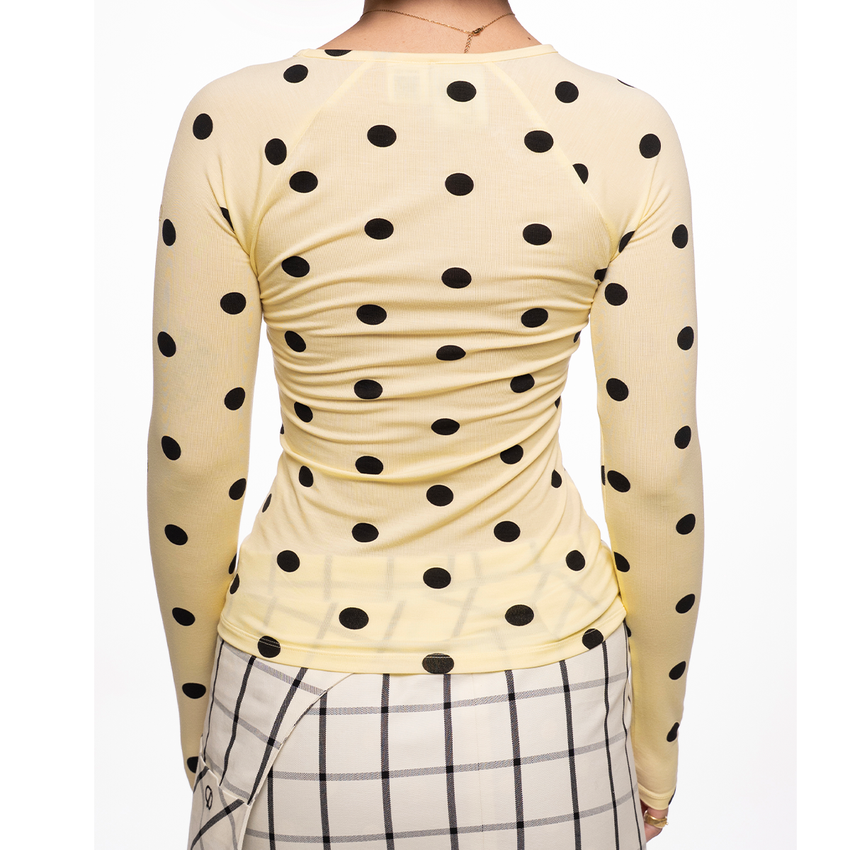 Yellow long-sleeve top with black polka dots worn by a person on a white background