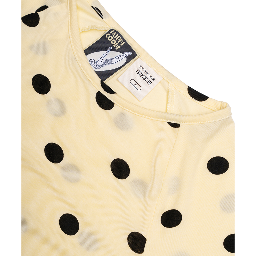 Yellow baby top with black polka dots and brand labels on a white background
