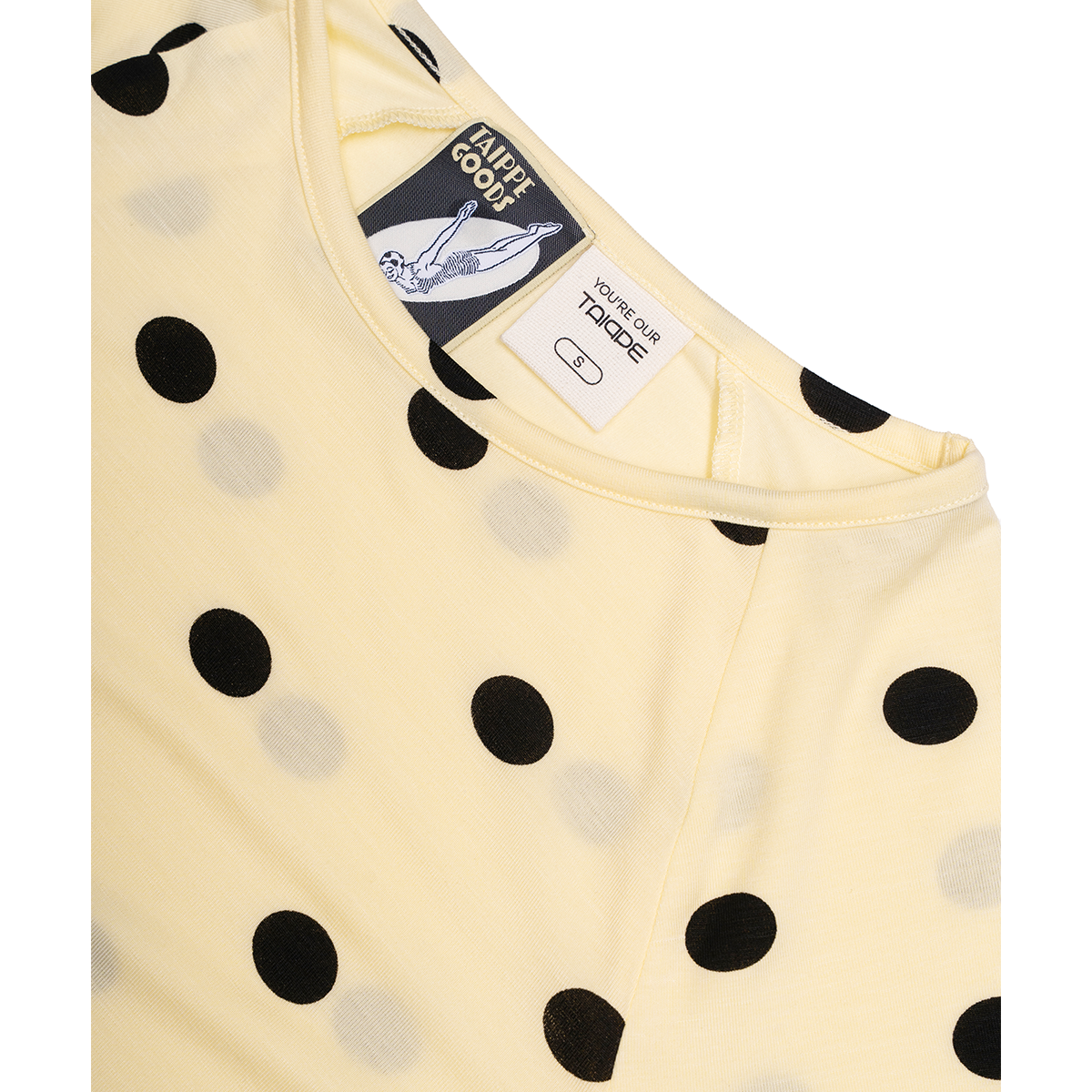 Yellow baby top with black polka dots and brand labels on a white background