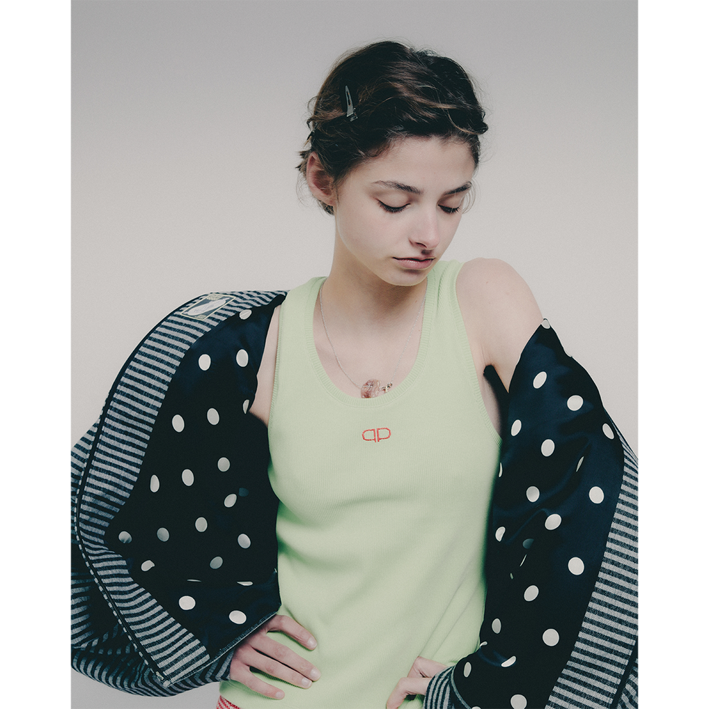 Woman wearing a light green tank top with a brand logo, with a striped jacket with polka dot lining on top