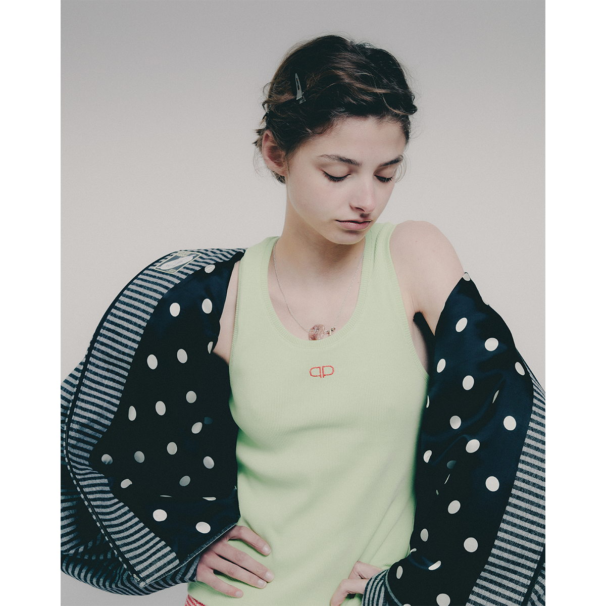 Woman wearing a light green tank top with a brand logo, with a striped jacket with polka dot lining on top
