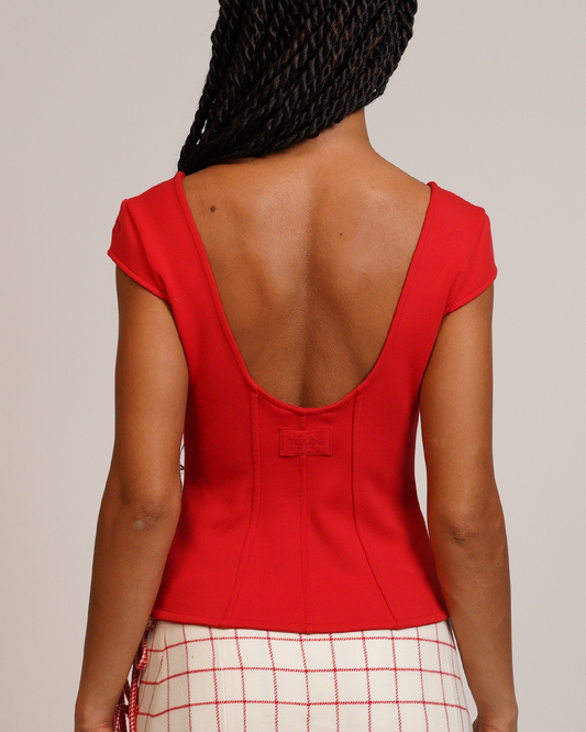 Person wearing a red top with an open back and plaid skirt on a plain background
