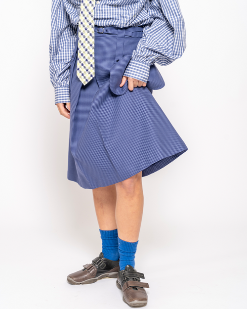 Person wearing a blue checkered shirt, tie, and skirt with blue socks on a white background