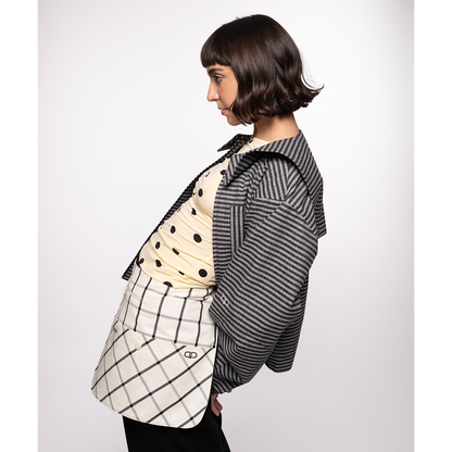 Person wearing a black and white striped jacket with a checkered belt bag on a plain background
