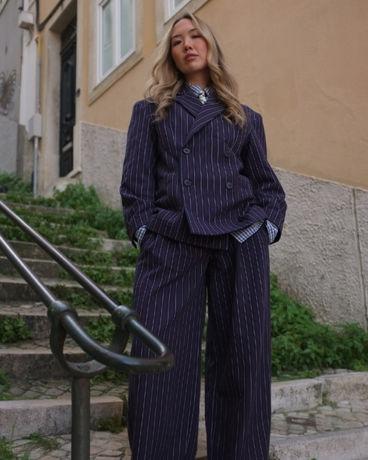 Woman in a pinstripe suit standing outdoors on a street.