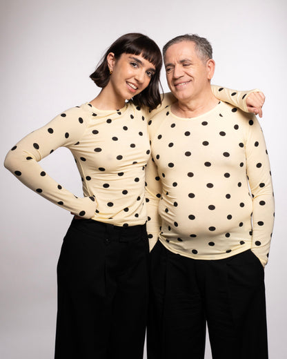 Two people wearing matching polka dot tops and black pants against a white background