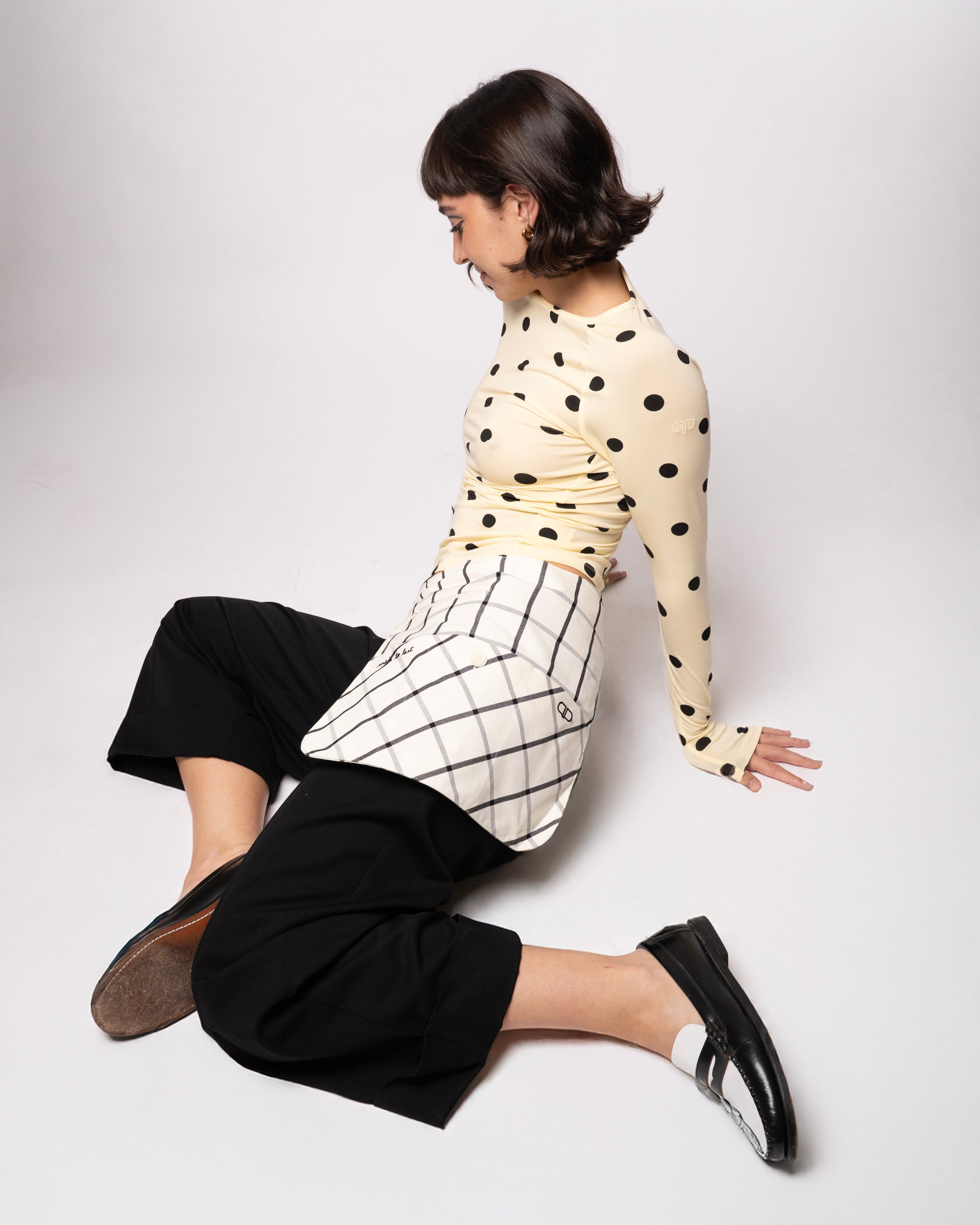 Person wearing a polka dot top and black pants on a white background