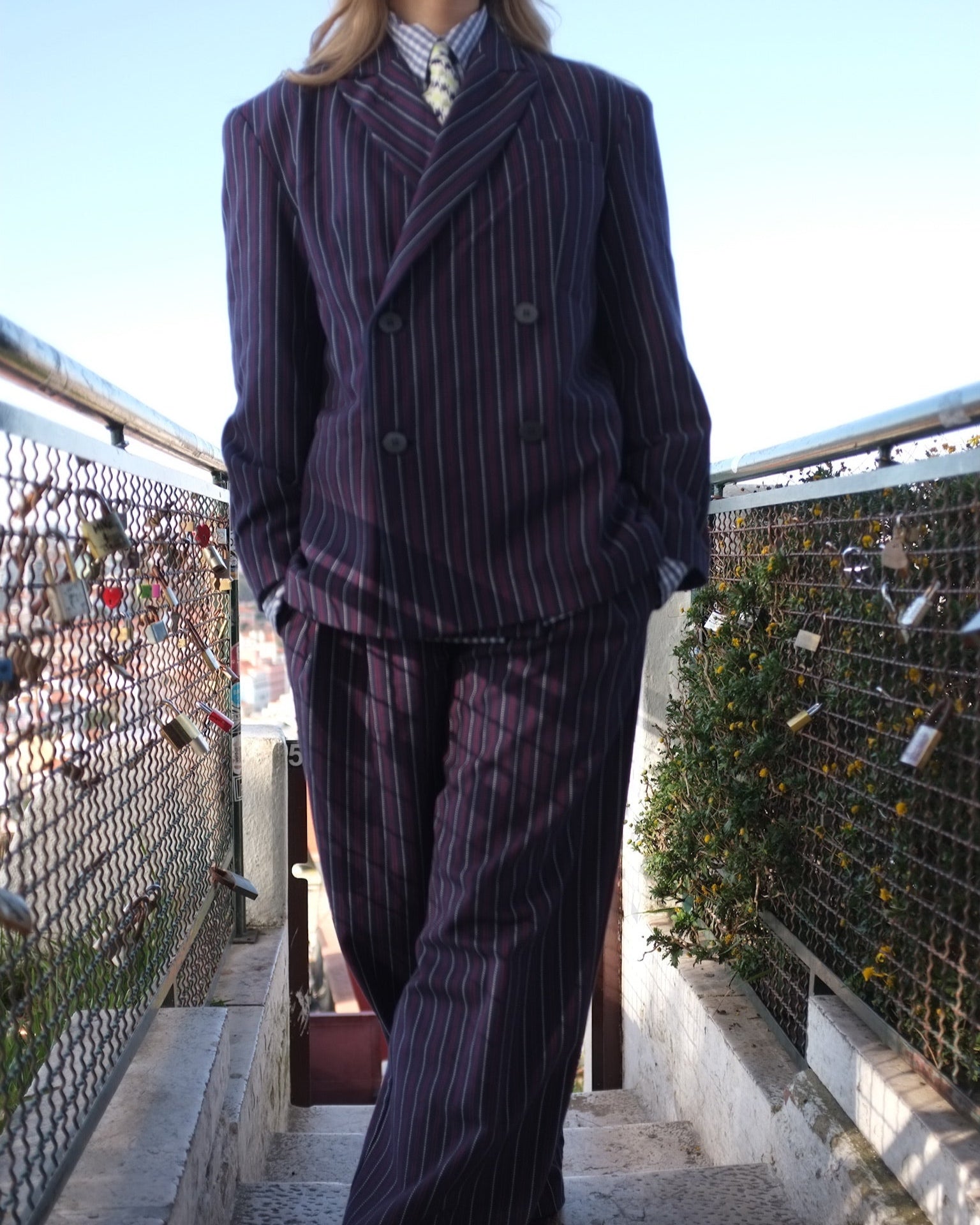 Person wearing a pinstripe suit standing on a bridge with a scenic background
