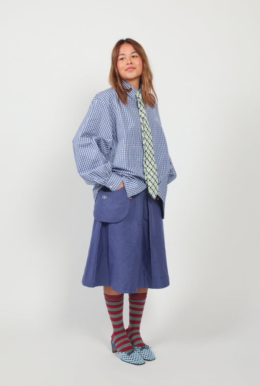 Person wearing a blue checkered shirt, blue skirt, and striped socks on a white background