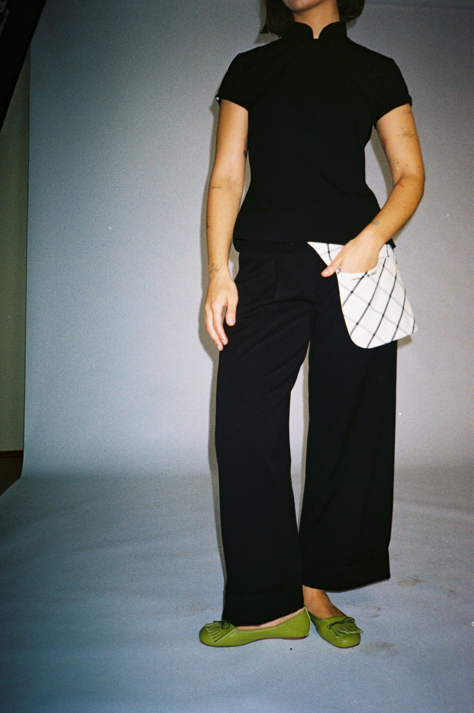 Person wearing a black outfit with green shoes on a plain background