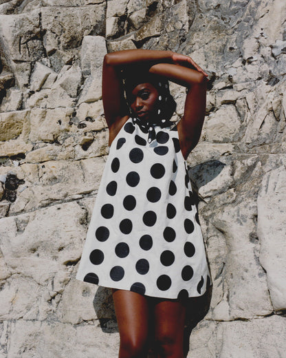 Woman wearing a black and white polka dot dress against a stone wall.
