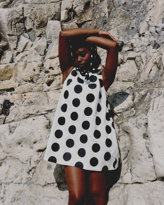 Woman wearing a black and white polka dot dress against a stone wall.