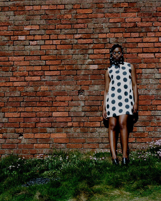 Woman in a polka dot dress standing against a brick wall.