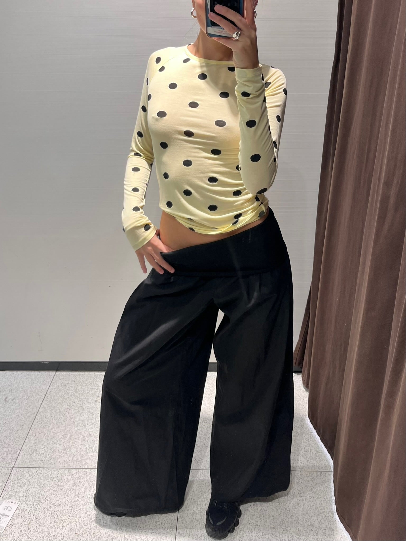 Person wearing a yellow polka dot long-sleeve top and black wide-leg pants in a mirror selfie.