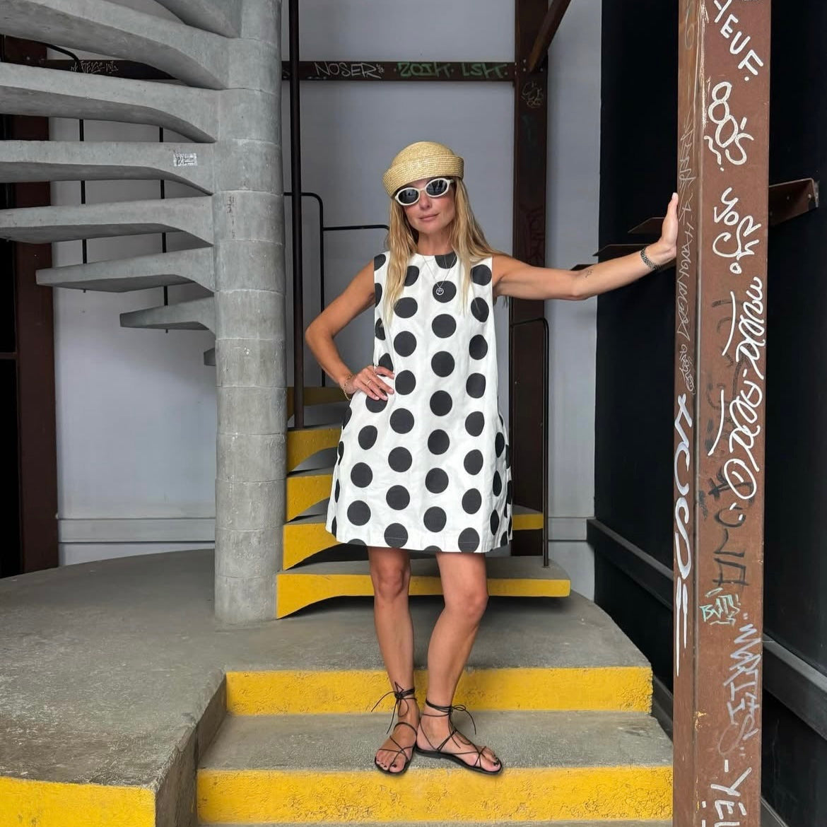 Woman in a polka dot dress standing on a staircase with graffiti on the wall.