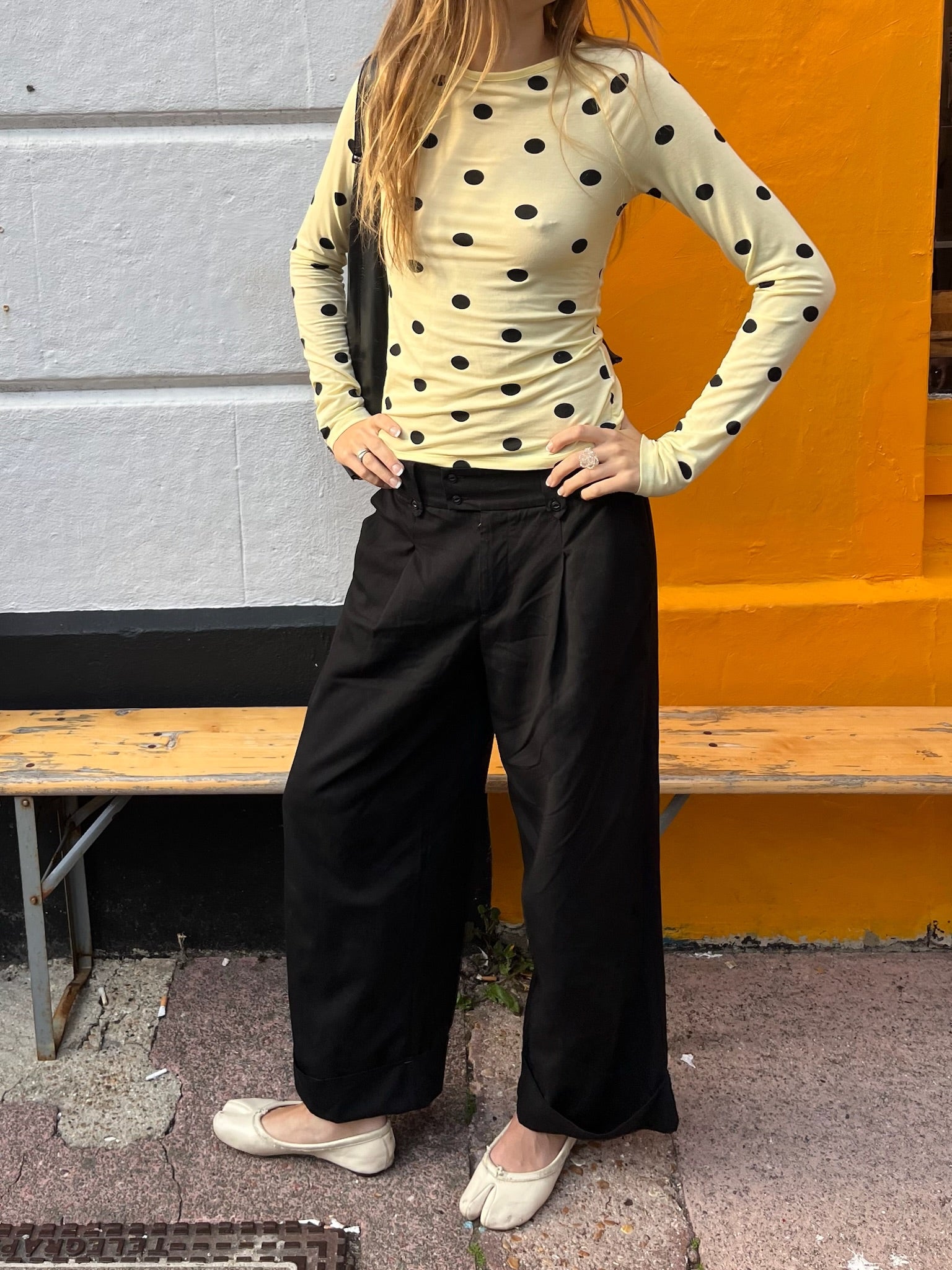 Person wearing a polka dot top and black pants standing against a colorful wall.