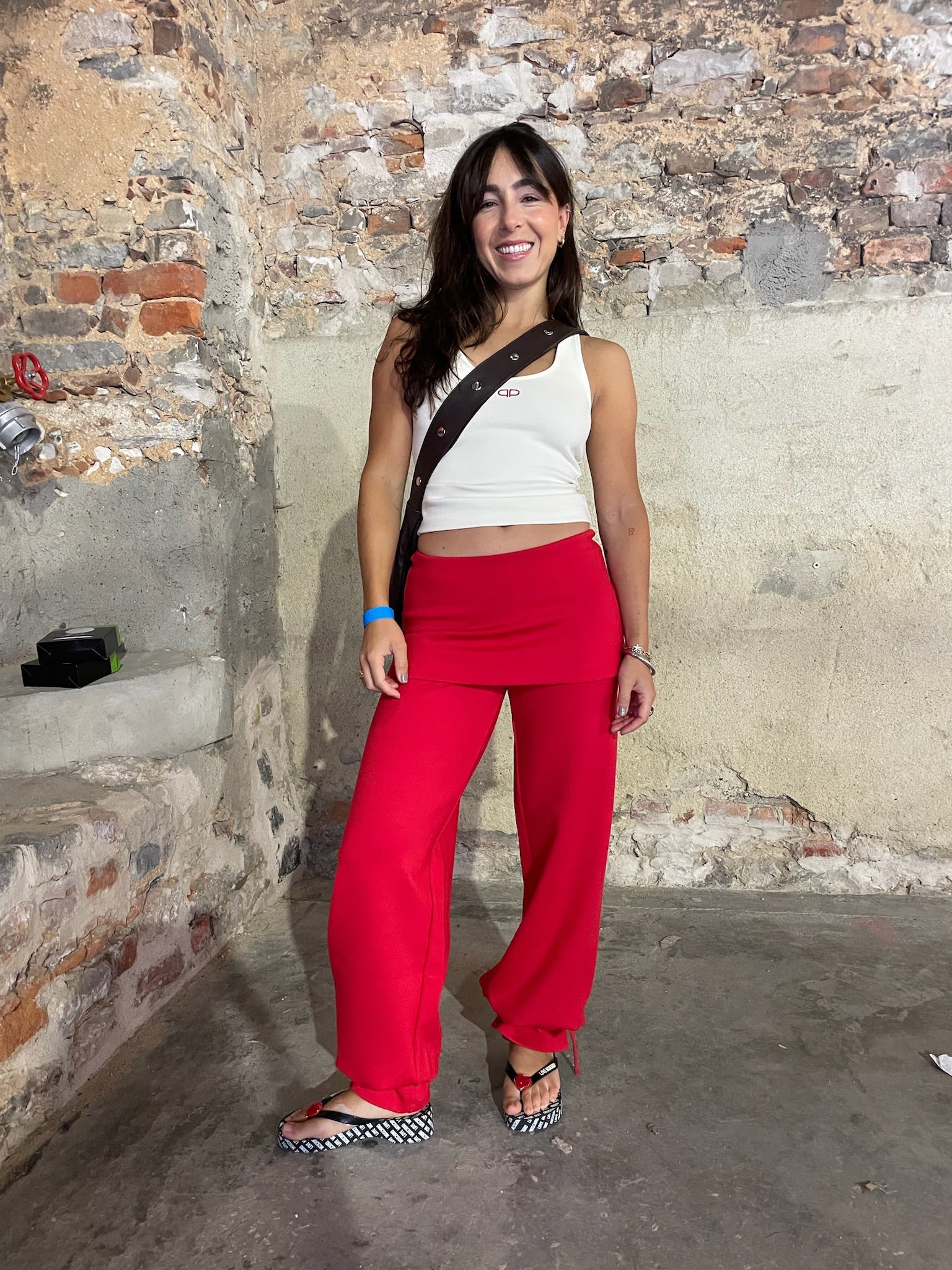 Woman wearing a white top and red pants standing against a textured wall.