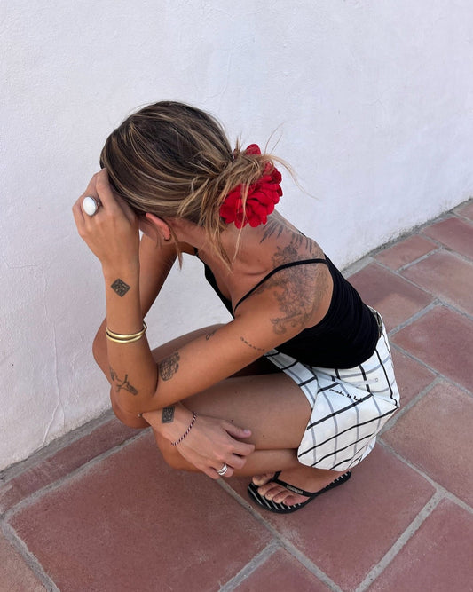 Woman squatting on a tiled floor with a white wall background with a checkered skirt 