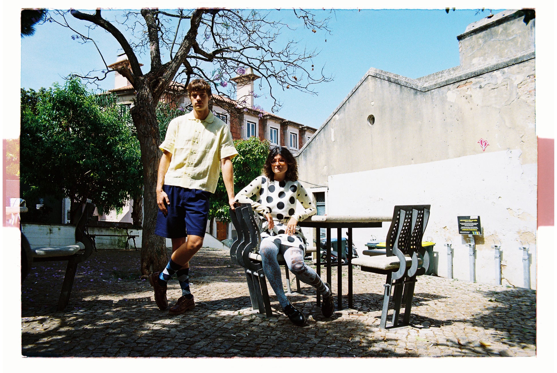 Two people sitting at a table outdoors with a building and tree in the background