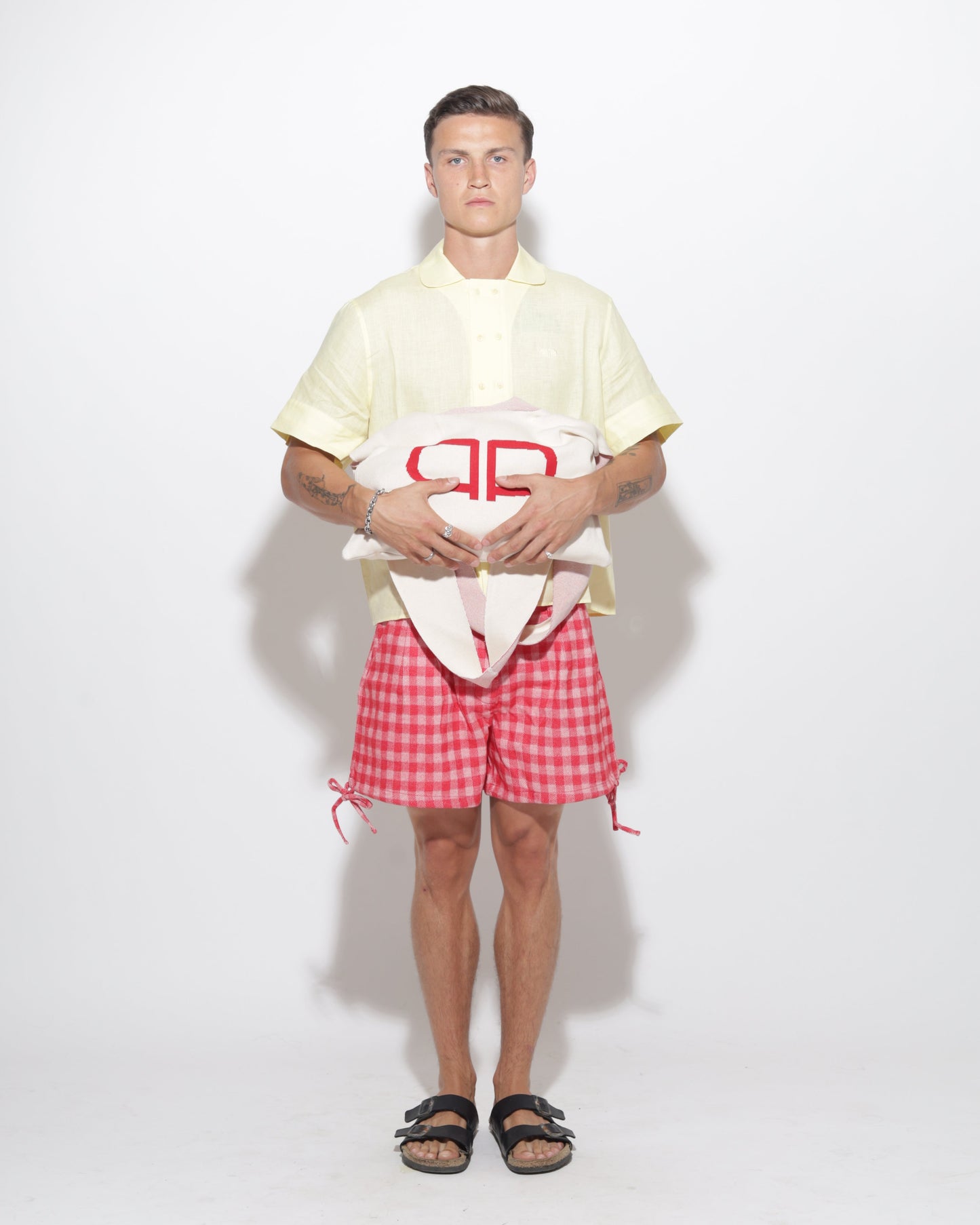 Person wearing a yellow shirt and  red checkered shorts on a white background