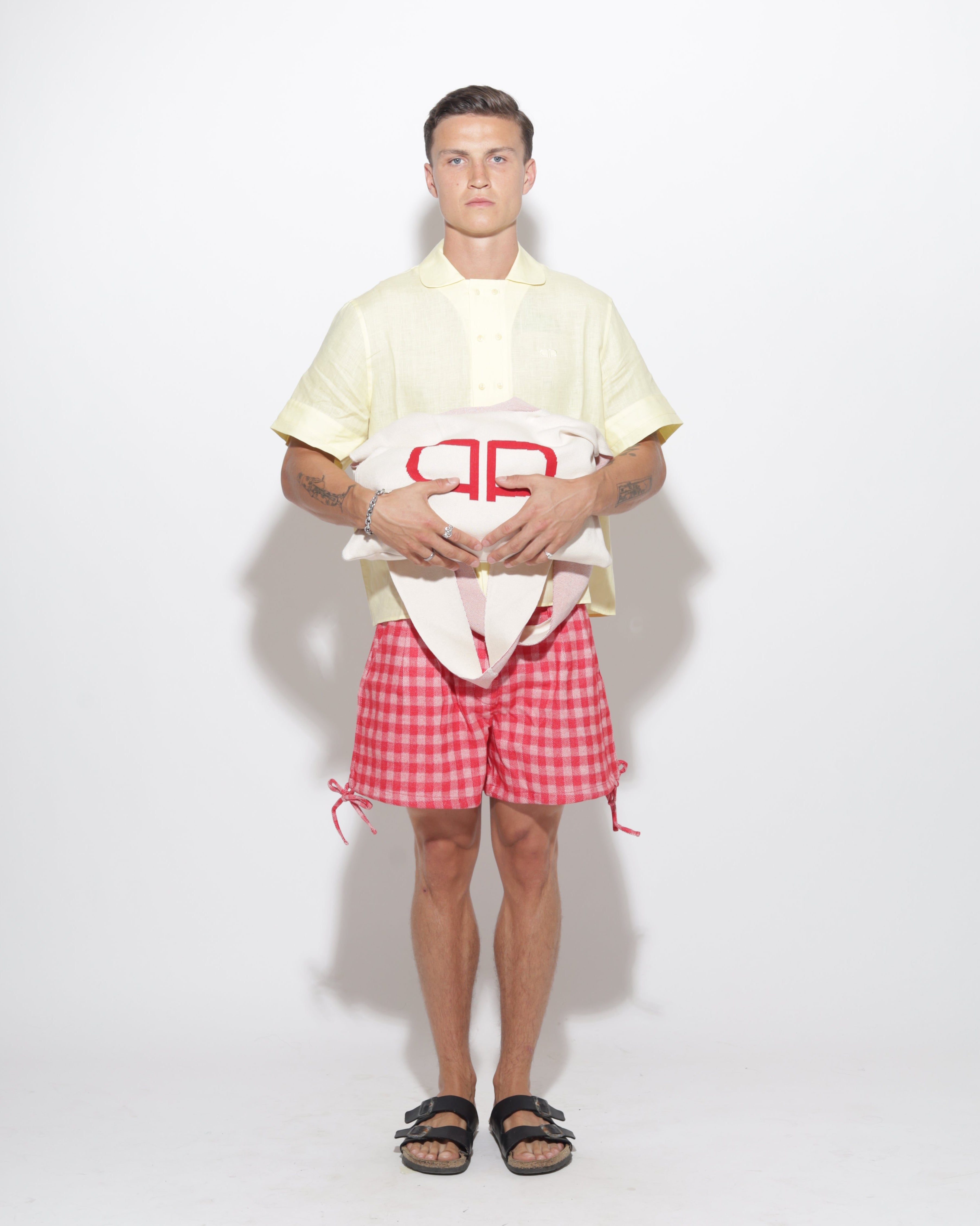Person wearing a yellow shirt and  red checkered shorts on a white background