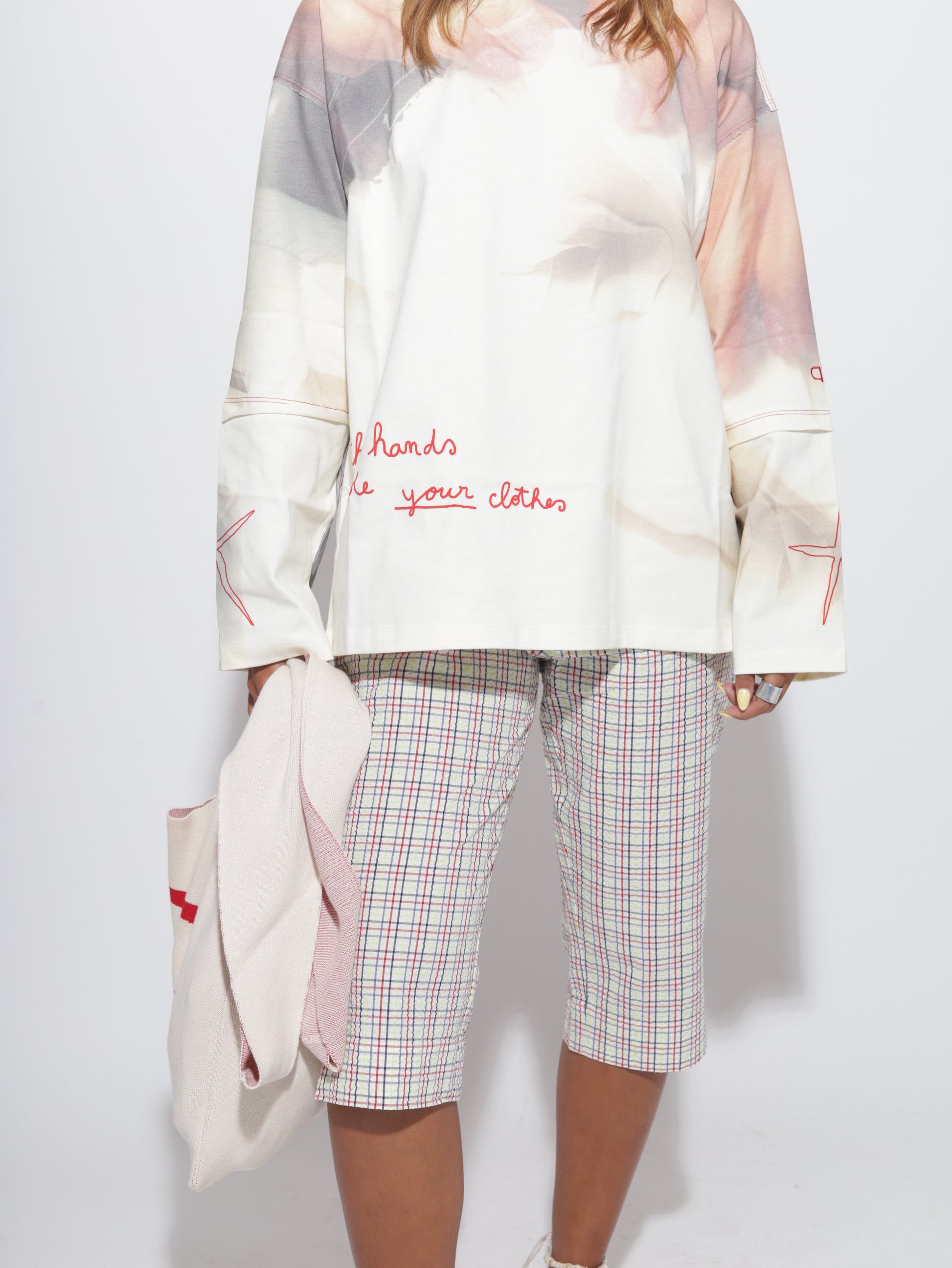 Person wearing a white top with text and plaid capris on a light grey background