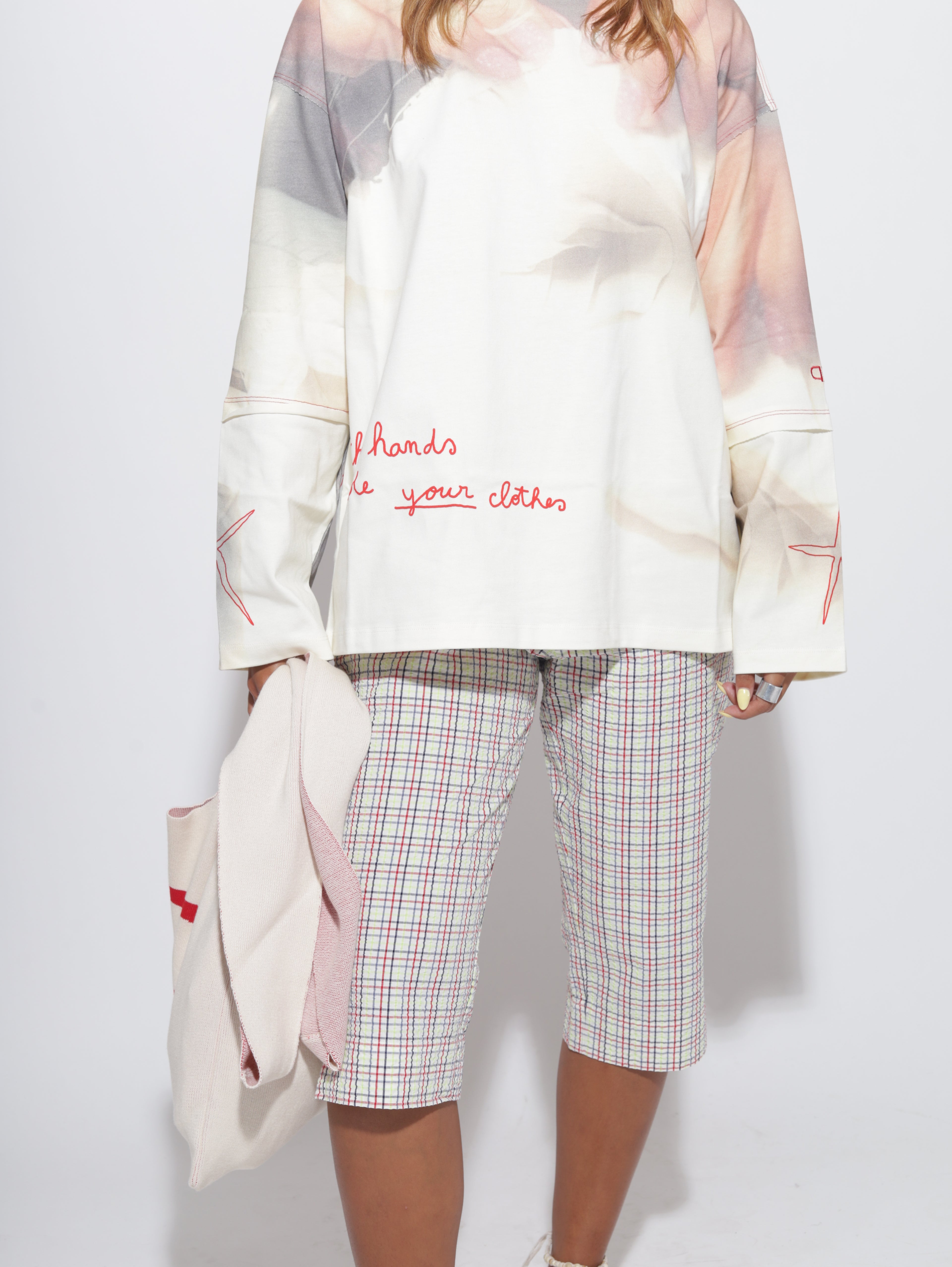 Person wearing a white top with text and plaid capris on a light grey background