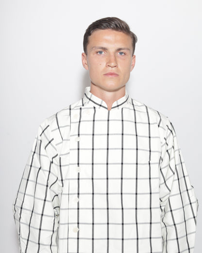 A portrait-style studio photograph of a man with short brown hair and blue eyes, wearing a white and black plaid jacket with a mandarin collar. The image is a close-up, showing his head and shoulders against a light background.