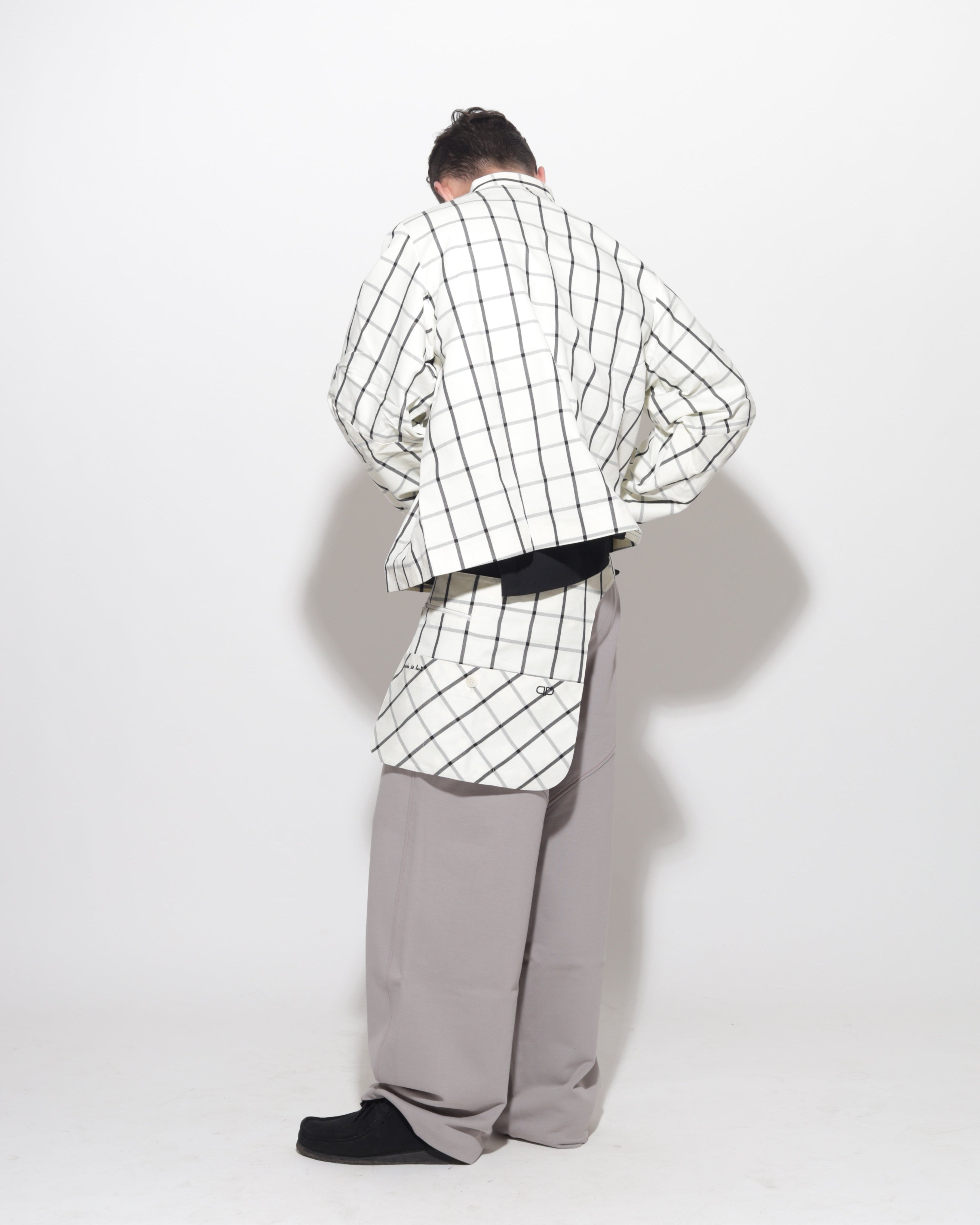 Person wearing a checkered jacket and gray pants on a white background