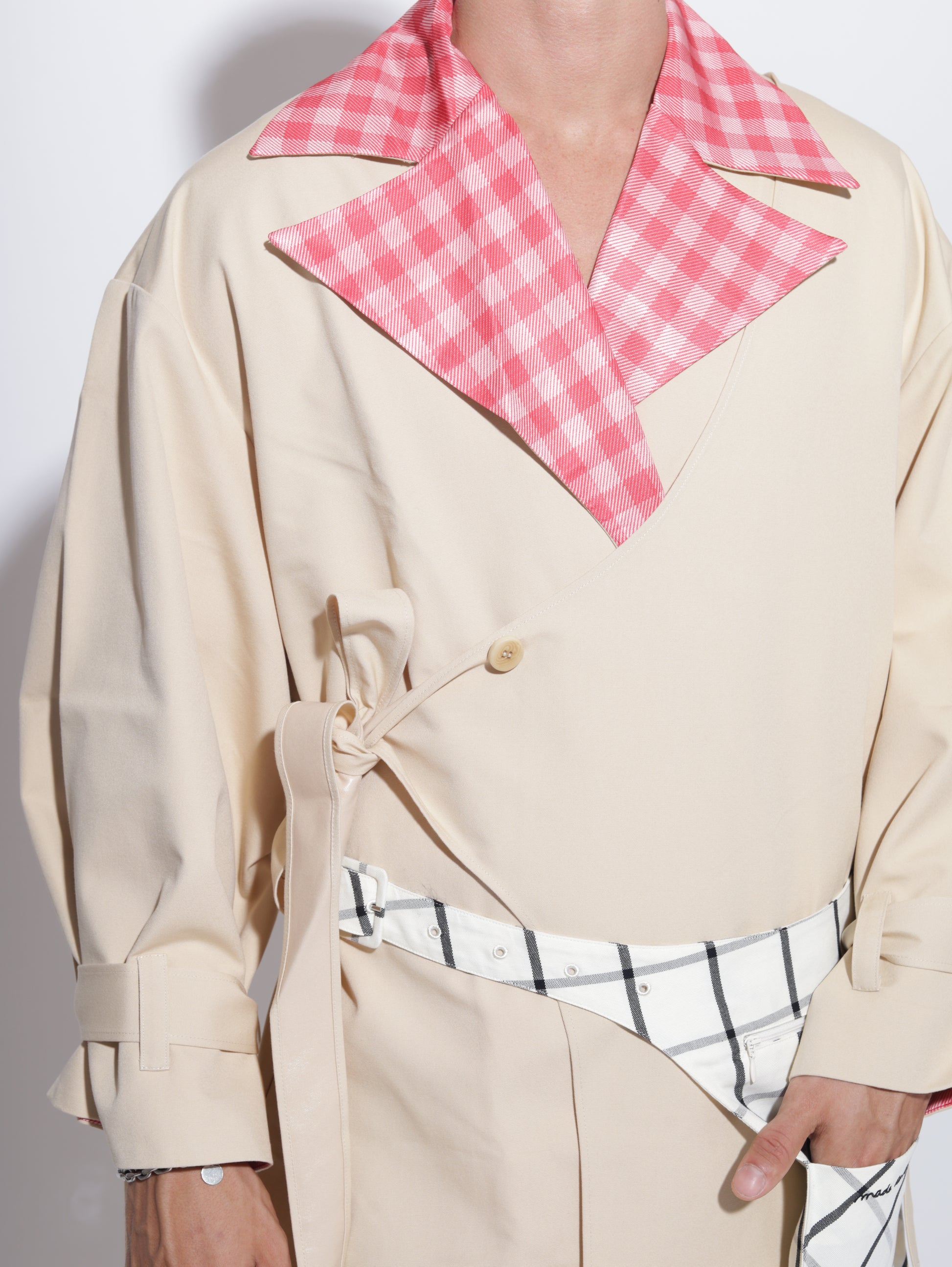 Person wearing a beige trench coat with a pink gingham collar