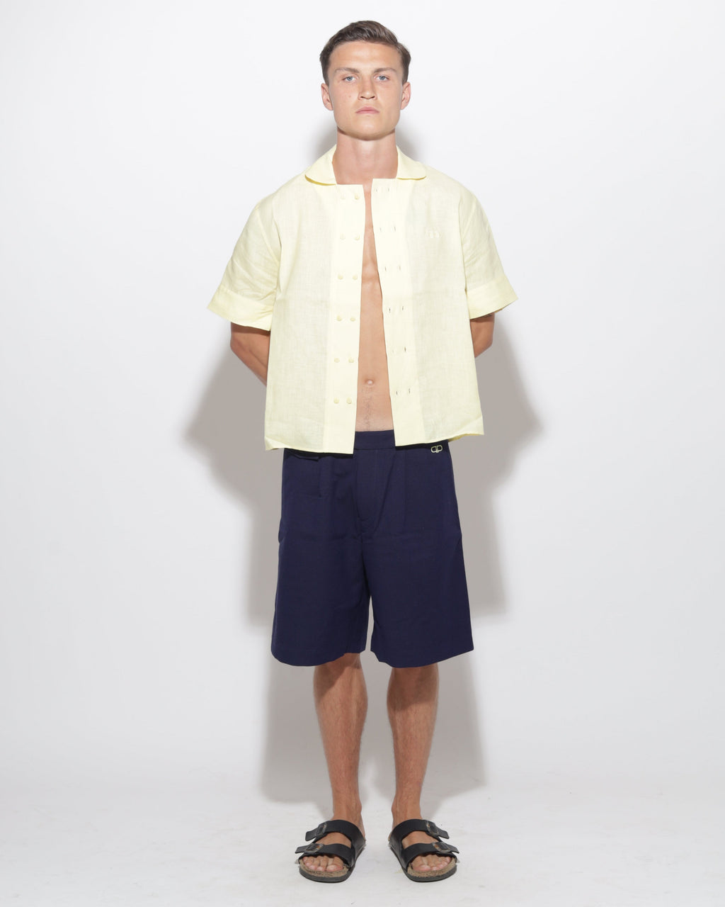 Man wearing a light yellow shirt and navy shorts on a white background